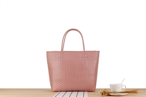 Detail of pink macaron woven plastic tote bag showing texture on a wooden table