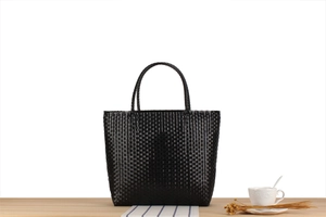 Detailed view of handwoven black plastic tote bag with smooth texture on a wooden surface