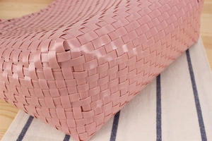 Detailed close-up of pink macaron woven bag texture on rustic wood and striped fabric