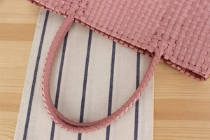 Close-up of pink macaron woven plastic handbag with detailed spiral braided handles