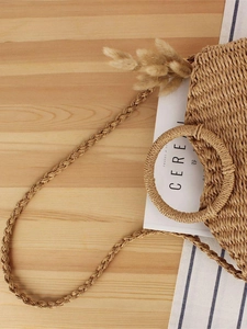 Handmade straw woven crossbody bag with round handles on a minimalist wooden background