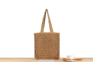 Detail of hand-woven straw tote bag with hollow knit pattern on wooden surface