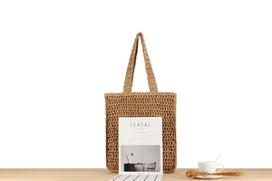 Detail of hand-woven hollow mesh straw tote bag with natural fiber texture on wood