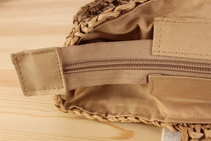 Detail view of woven straw bag showing the smooth zipper closure and fabric lining