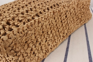 Detailed close-up of the intricate cross-weave texture on a brown woven straw handbag