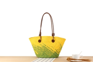 Detail der handgewebten Strohtasche mit Farbverlauf, braunen Henkeln und Urlaubsdekor