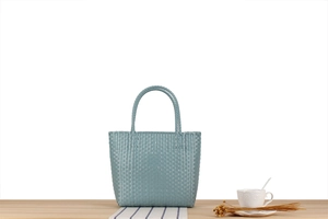 Detail of light green woven plastic tote bag with sturdy handles on a picnic table