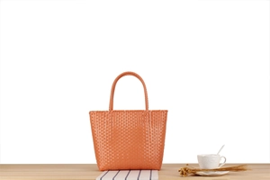 Detail of a bright orange woven tote bag on a wooden table with a cozy picnic aesthetic