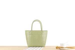 Detail view of a light green woven tote bag with a ring handle on a wooden table