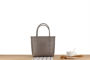 Macro view of woven taupe tote bag texture with cylindrical double handles on wooden desk