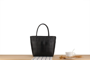 Macro detail of hand-woven black glossy texture on minimalist trapezoid handbag