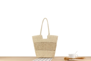 Detail view of a hollow woven tote bag in cream paper rope on a minimalist wooden table