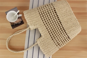 Detail of hollow woven paper rope tote bag in beige on a rustic wooden table for summer