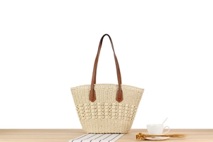 Detailed close-up of woven beige tote bag with brown leather straps on wood surface