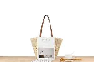 Close-up of woven straw tote bag with brown faux leather handles on a wooden table