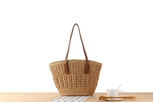 Close-up of woven straw tote bag featuring brown leather handles and hollow mesh texture