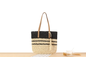 Détail du sac en paille tissé à rayures avec anses en cuir marron et pompon décoratif