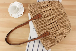 Macro view of woven straw tote texture with brown leather strap and white stitching
