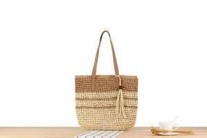 Détail du sac cabas en paille rayé avec anses en cuir et pompon sur table en bois