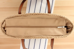Detail view of woven straw tote bag featuring brown leather handles and secure zip closure
