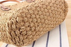 Detailed macro view of woven straw base and leather handle accents on beach tote bag