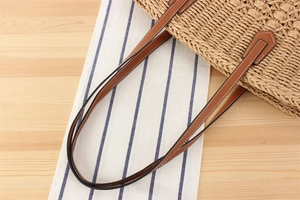 Macro view of woven straw tote bag with brown leather handles and white contrast stitching