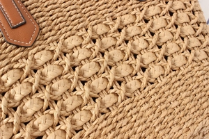Close-up of woven straw tote bag with brown leather handles and white contrast stitching