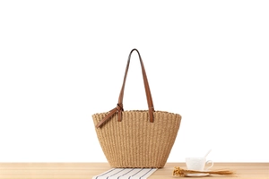 Detail of woven straw tote bag with brown leather handles on a minimalist table