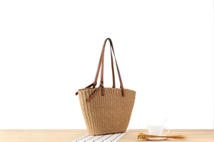 Detail of hand-woven paper rope tote bag with brown leather handles and decorative knots