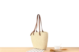 Close-up of beige woven paper rope texture with brown leather handles on a minimalist beach bag