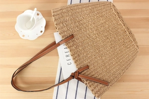 Detail of woven tote bag with brown leather handles and decorative knots on wooden desk