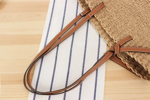 Detail of woven straw tote bag with brown leather handles and decorative bow accent