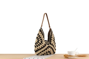 Detail of hand-woven geometric pattern hobo bag with brown leather strap on wooden table