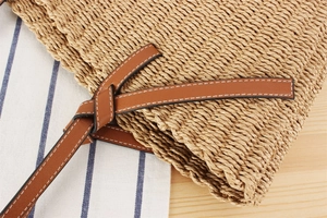 Close-up of woven paper rope bag with brown leather strap and white stitching details