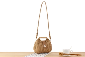 Detail of paper rope woven bag with brown leather flap and gold metal clasp on table