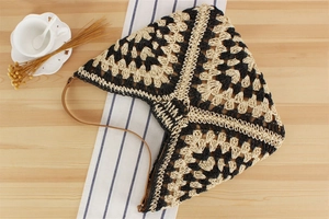 Detail of hand-woven tote bag with geometric pattern and brown leather strap on wooden table