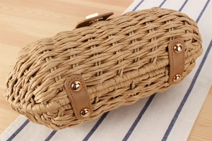 Detailed close-up of woven paper straw bag bottom with brown leather and gold studs