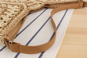 Detail of woven straw tote showing geometric patterns and faux leather strap attachment