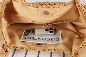 Detail view of woven straw tote bag featuring fabric lining, zipper pocket, and magnetic closure