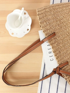 Large woven paper rope tote bag with brown leather handles on a minimalist wooden surface