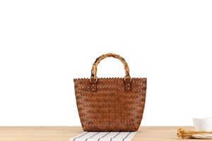 Detail of a hand-woven beach bag featuring a brown vintage bamboo handle and retro design