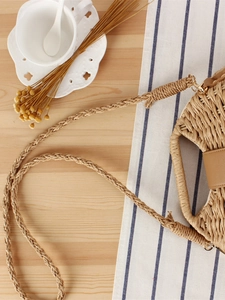 Handwoven straw shoulder bag with leather accent on a rustic wooden table setting