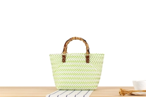 Detailed view of woven straw beach bag with retro bamboo handle and green chevron pattern