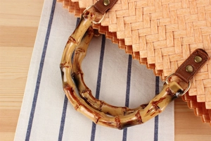 Detail of bamboo handle and leather buckle on orange woven retro summer beach handbag