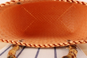 Detail of orange woven handbag with bamboo-style handle and golden D-ring hardware
