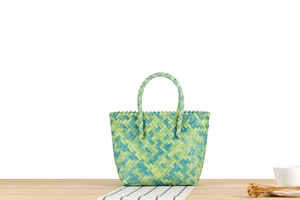 Detail of hand-woven green and blue patterned beach bag on a wooden table with accessories