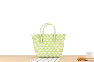 Detail of green and white woven handbag with double handles on a wooden table