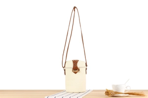Detail of cream straw cylinder bag with brown leather strap and gold metal twist lock