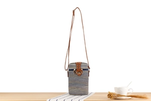 Detail of striped paper rope woven cylinder bag with leather flap and gold clasp