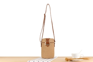 Detail of a cylindrical straw bag with brown leather strap and golden rotating metal clasp